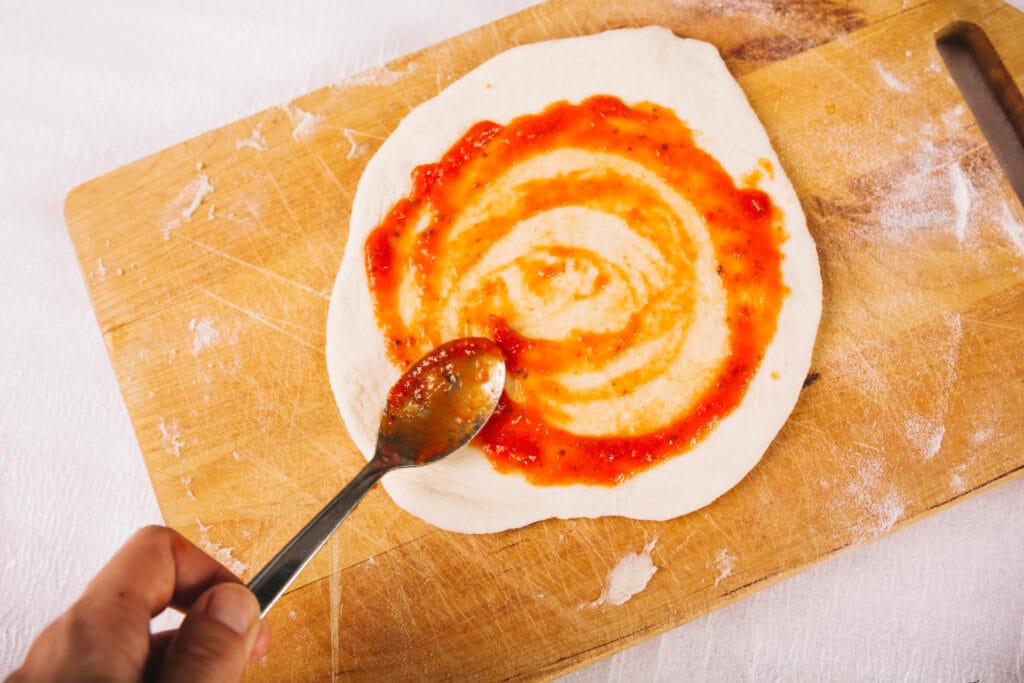 crop hand smearing sauce pizza